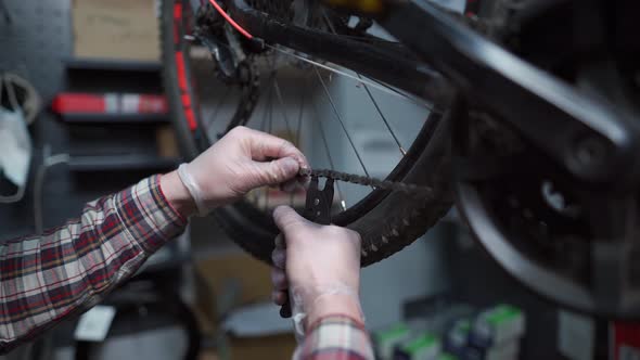 Hands of a Male Bicycle Mechanic in Work Clothes Opens the Lock of a Bicycle Chain with a Special