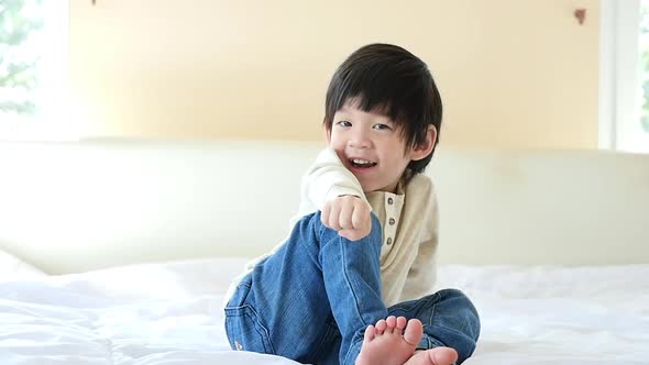 Cute Asian Child Sitting On White Bed