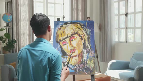 An Asian Artist Man Holding Paintbrush And Thinking Before Painting A Girl's Hair On The Canvas