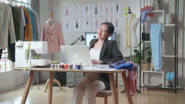 Female Designer In Business Suit Working On A Laptop And Having A Backache While Designing Clothes