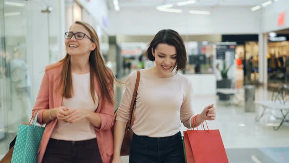 Attractive Young Women Are Walking in Shopping Center with Bags