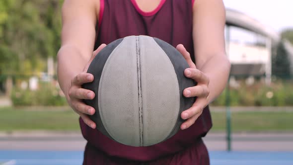 A Guy Basketball Player Holds a Ball in His Hands and Holds It Out To the Camera. Outdoor Training