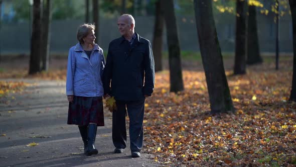 Old Woman Is Walking with Her Husband in Park at Fall Day, Spouses Are Enjoying Good Weather