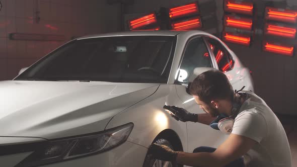 Man Checks Result of Polishing of Car with a Flashlight