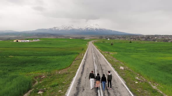 Young Travelers Walk Along An Empty Asphalt Road. Aerial View.