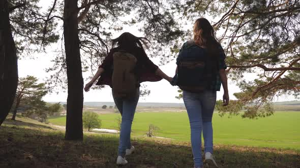 Women Tourists Go Through Forest. Sexy Female Travelers with Backpacks Straighten Their Arms To Side