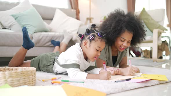 4K Little African girl sibling lying on the floor drawing and painting on paper book together.