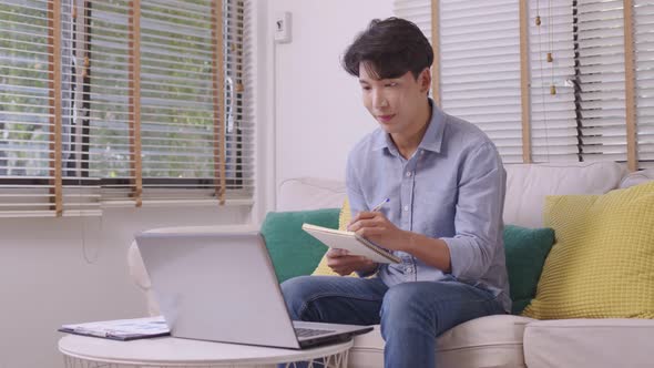 At home, an Asian businessman works on a desk with a laptop, searching for jobs and paperwork.