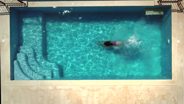 Aerial view of young woman diving into swimming pool.