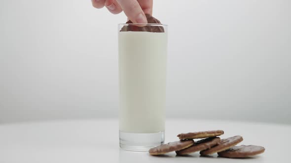 Closeup Glass of White Milk with Female Hand Dipping Cookie in Drink Leaving