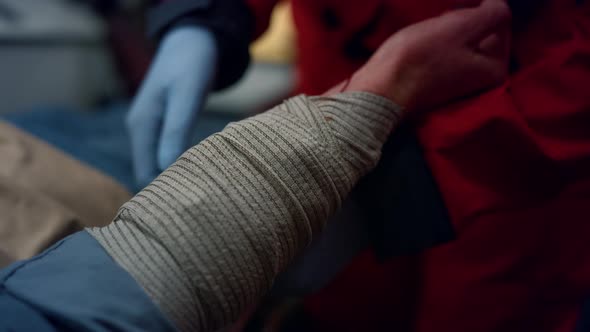 Closeup Ambulance Paramedic in Gloves Wrapping Patient Hand with Elastic Bandage