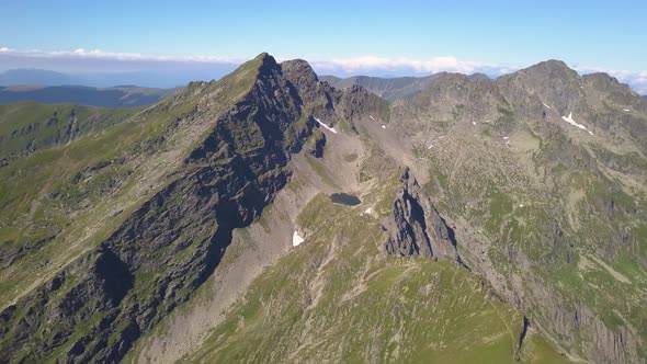 High altitude aerial panorama from drone hovering high over jagged mountain peaks. Blue sky and clou