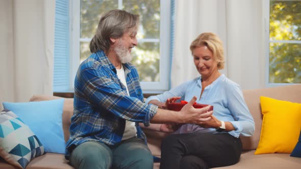 Mature Husband Presenting Packing Gift for Wife Sitting Together on Couch at Home