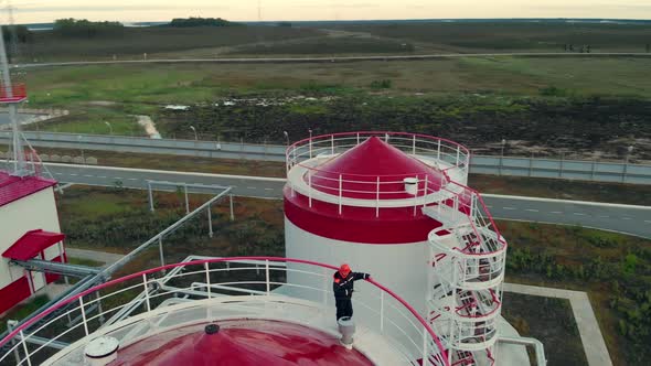 The Drone Flies Around the Tanks with Oil on Top of an Employee in a Helmet Talking on a