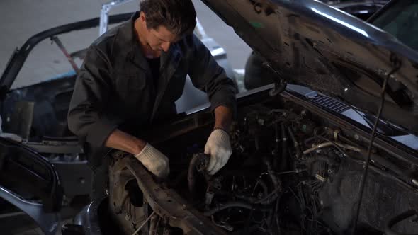 Waist up portrait view of the serious car mechanic in his repair shop standing next to the car.