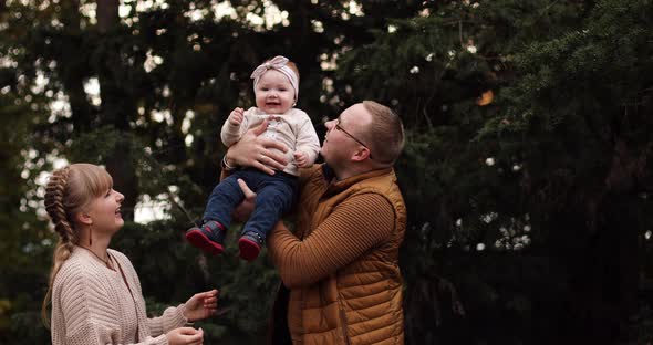 Loving Mother Kissing Her Daughter on Father's Hands in Park.