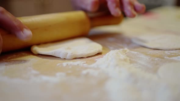 Female Hands Roll Out a Piece of Dough for a Pie with a Rolling Pin