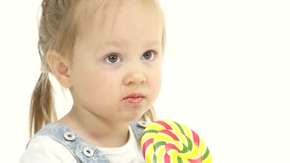 Child Is Holding a Sweet Candy in Her Hands and Licks It. White Background. Close Up. Slow Motion