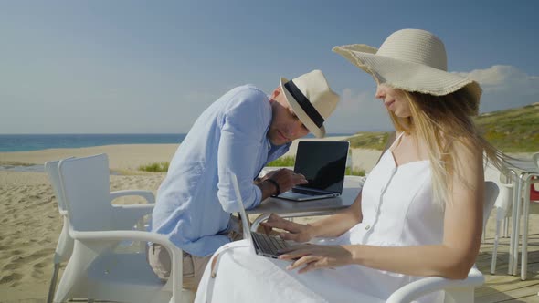 Couple Talking and Using Laptops on Beach