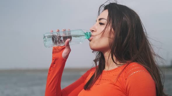 Beautiful sportswoman drinks water. Attractive sports girl drinks water on the street after a workou