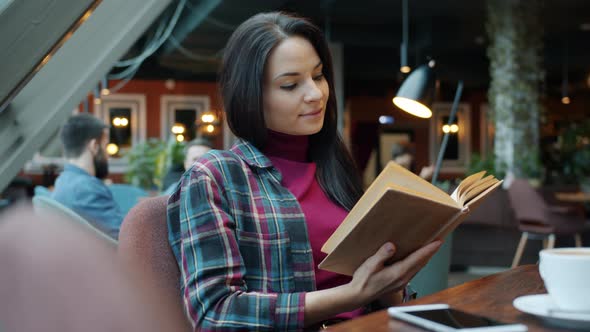 Attractive Girl Reading Interesting Book in Cafe Relaxing Sitting at Table Alone Turning Page