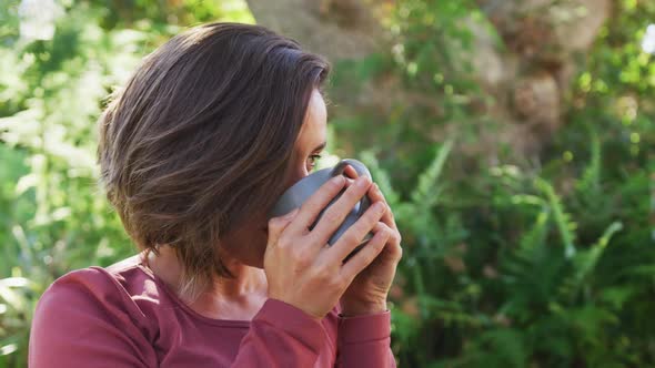 Smiling caucasian woman drinking tea sitting in sunny garden