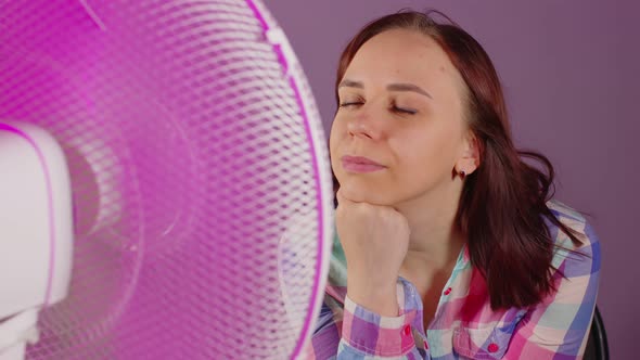 Close Up of Young Woman Sitting on Chair in Front of Fan on Purple Background