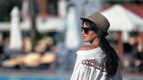 Trendy Tanned Brunette Woman in Straw Hat and Sunglasses Relaxing Swimming Pool Waterfall