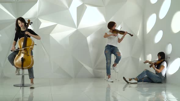Two Girls Playing the Violins One on the Cello in the White Studio