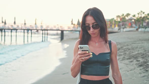 Woman with Phone Walks Barefoot Along Shore Beach and Walks Along Sea