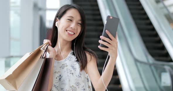 Woman talking on cellphone with video call and holding shopping bags