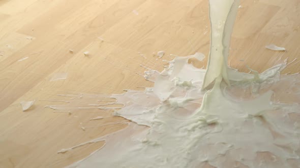 Dropping glass of milk and breaking on wooden floor, Slow Motion alt