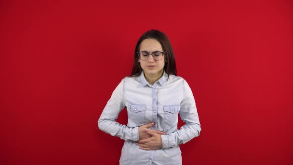 A Young Woman with Glasses Has a Stomach Ache and She Holds It in Her Hands