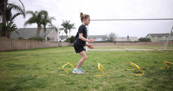 A young athletic girl does two footed hops over speed hurdles as part of her soccer warm up.