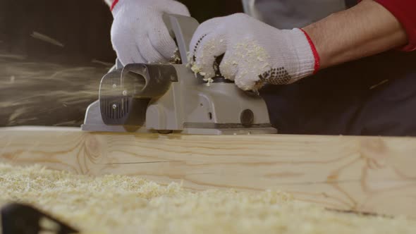 Close-up Hands of Carpenter Using Electric Planer with Wooden Blank in Workshop.