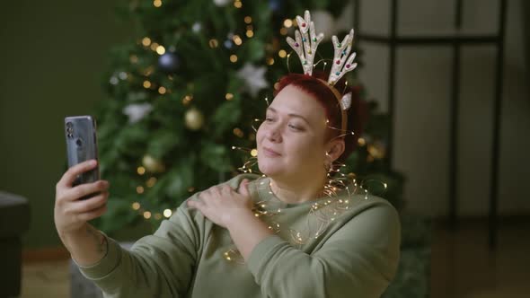 Plump woman decorates herself in Christmas decor, takes selfie in smartphone