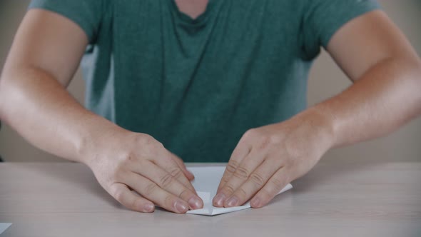 Man Is Folding a Paper Airplane on the Table