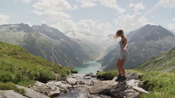 A girl in a white dress jumps across a little stream from right to left. The scenery looks like a fa