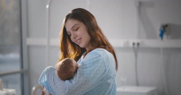 Portrait of Happy Mother Rocking Sleeping Baby in Hospital Ward