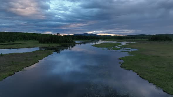 Blue hour aerial flying over river floodplain reflection clouds