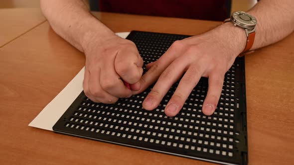 A Man Uses a Special Stencil and Stylus to Write a Letter in Braille