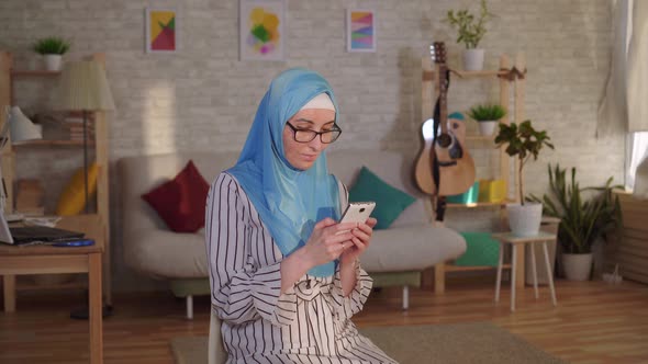 Young Muslim Woman in Hijab with a Scar From a Burn on Her Face Uses a Smartphone