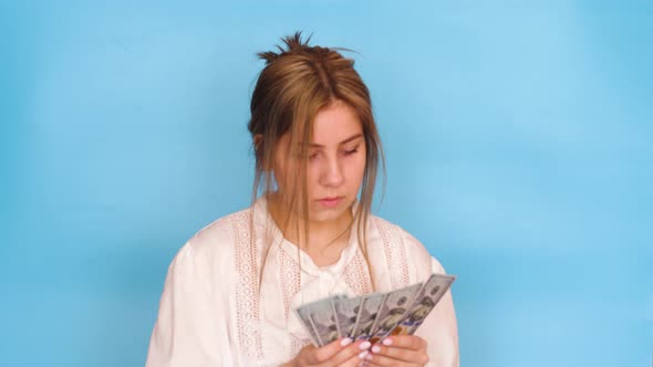 Serious pensive Caucasian young woman 20 years old in a white blouse counts paper bills of 100 dolla