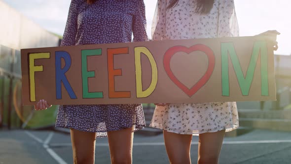 Video of two women standing with billboard and holding hands. Shot with RED helium camera in 8K.