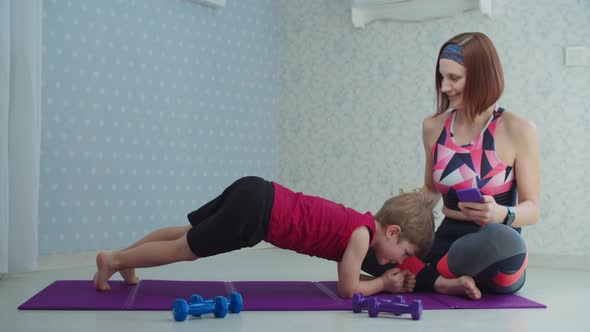 Family making sports at home. Mother in sportswear helping preschooler son to do plank exercise