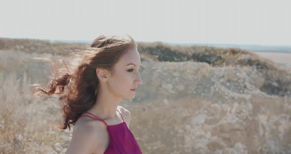 Woman with Blowing Hair in Dress Looks Far and Raises Head to Sky Among Cliffs