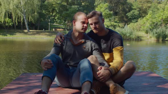 Loving Gay Couple Resting on Wooden Pier By Lake