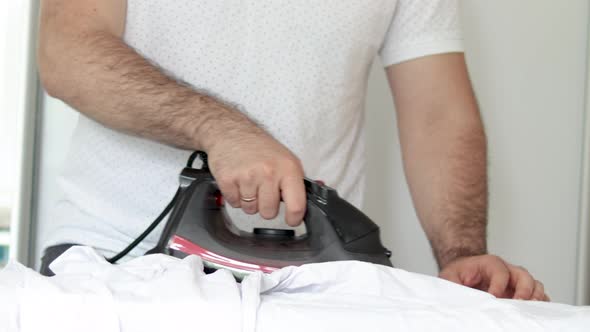 man is ironing a white shirt.black iron.multitasking husband is doing home stuff.wardrobe background