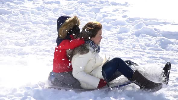 Asian Mother And Her Son  Sliding On Sleds Down Snow Hill In Winter