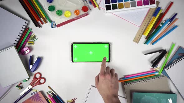 Man is Swiping Left Then Tapping on the Smartphone with Green Screen Lying Among Stationery alt